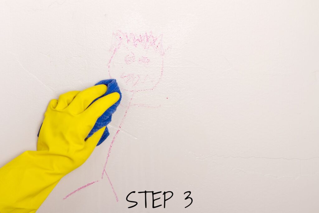 mano enguantada fregar dibujo de un niño de la pared de yeso antes de pintar